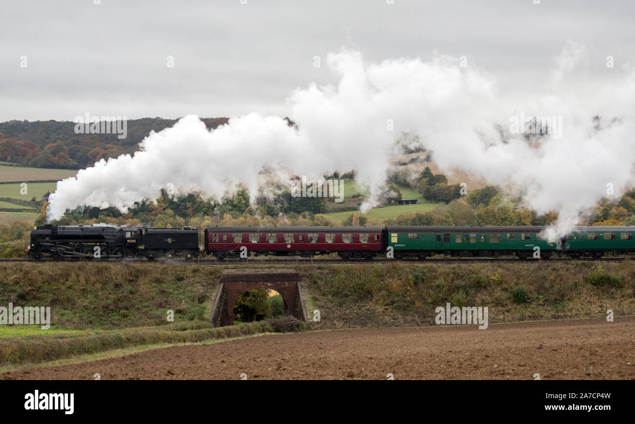 Le ferrovie britanniche standard di classe 9F locomotiva a vapore tira un treno lungo la metà Hants railway, noto anche presso la "linea di crescione', vicino a Ropley in Hampshire. Foto Stock