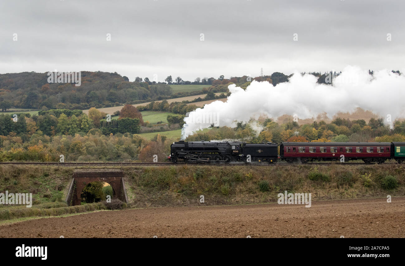 Le ferrovie britanniche standard di classe 9F locomotiva a vapore tira un treno lungo la metà Hants railway, noto anche presso la "linea di crescione', vicino a Ropley in Hampshire. Foto Stock