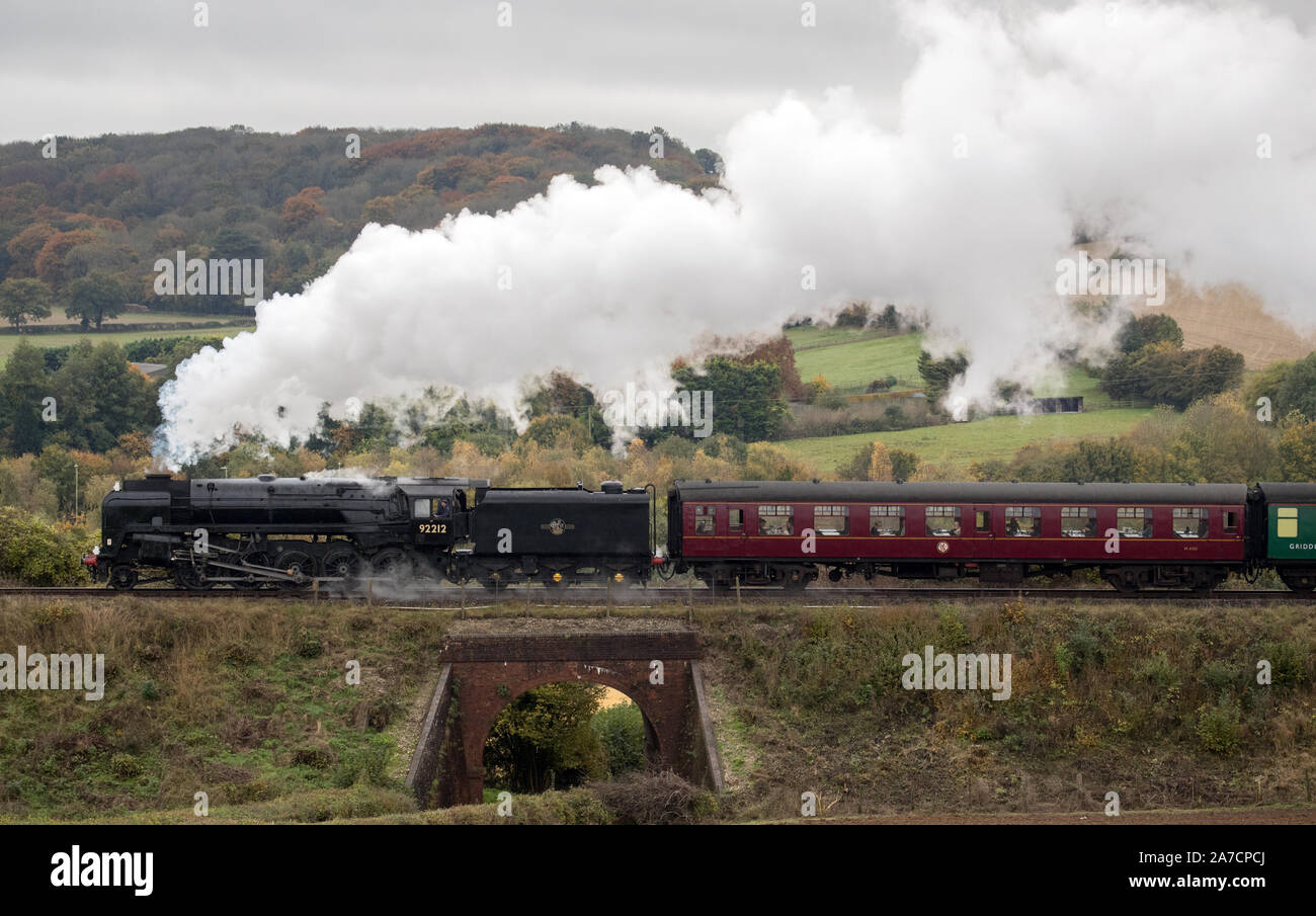 Le ferrovie britanniche standard di classe 9F locomotiva a vapore tira un treno lungo la metà Hants railway, noto anche presso la "linea di crescione', vicino a Ropley in Hampshire. Foto Stock