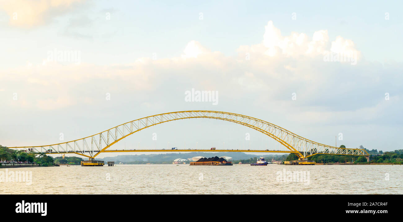 Kutai Kartanegara ponte che attraversa il fiume Mahakan in Tenggarong, Kalimantan orientale, Indonesia. Rimorchiatore trascinare la chiatta sotto il ponte Foto Stock