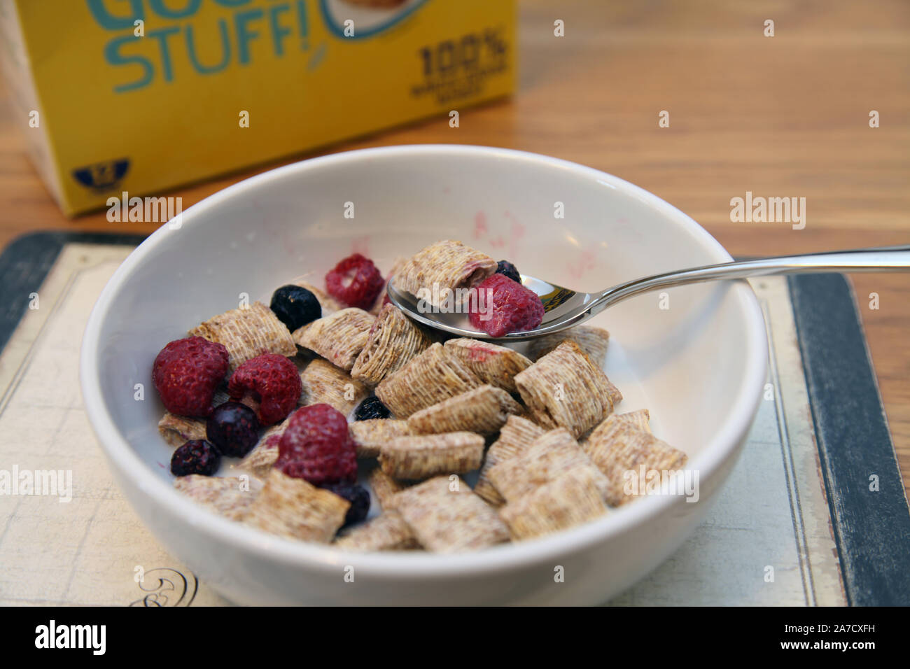Taglia di morso di grano trinciato con bacche di frutta in ciotola bianca con cucchiaio a colazione Foto Stock