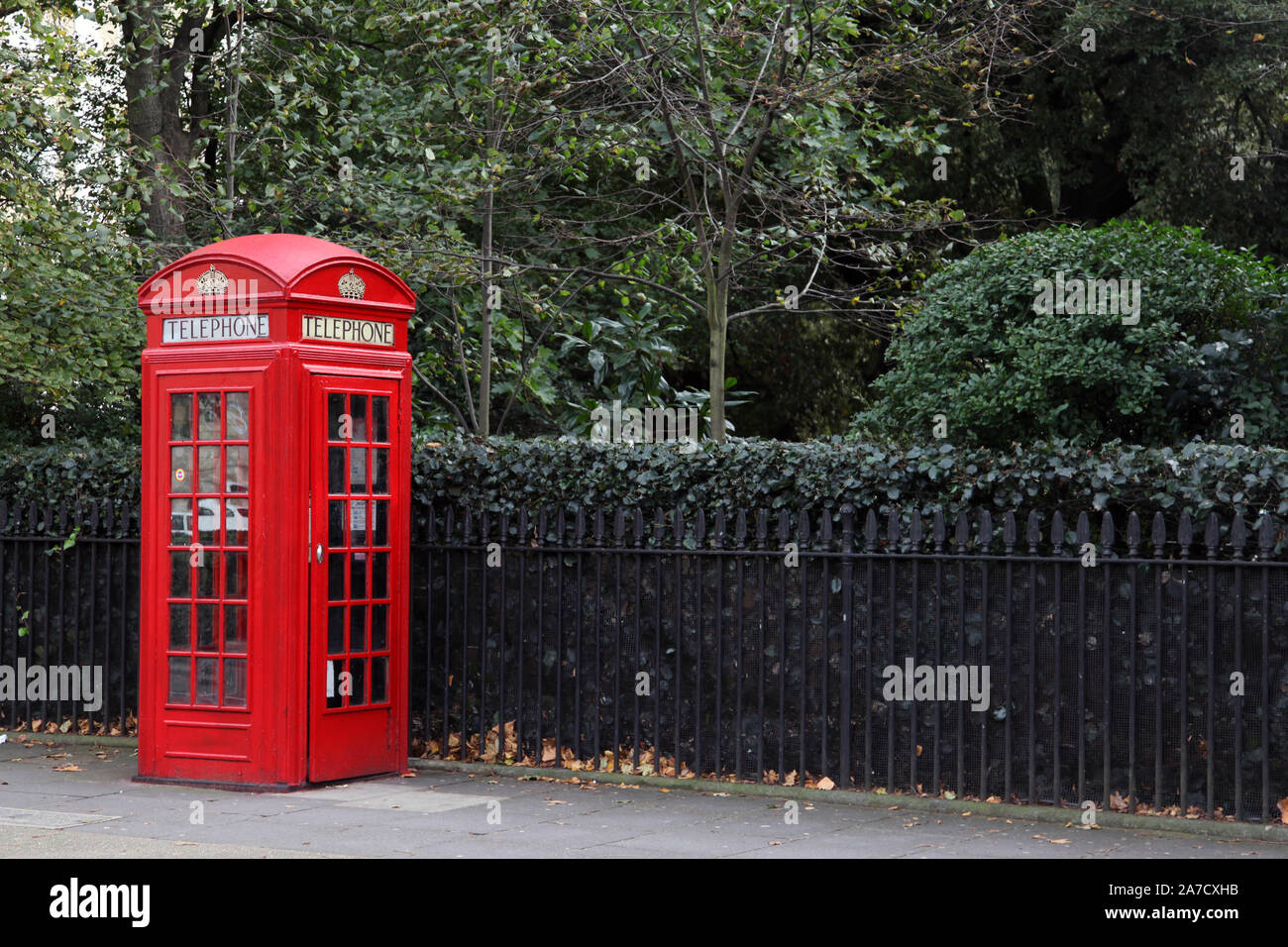 Una scatola telefonica rossa K2 su una London Street con ringhiere e verde dietro con spazio di copia Foto Stock