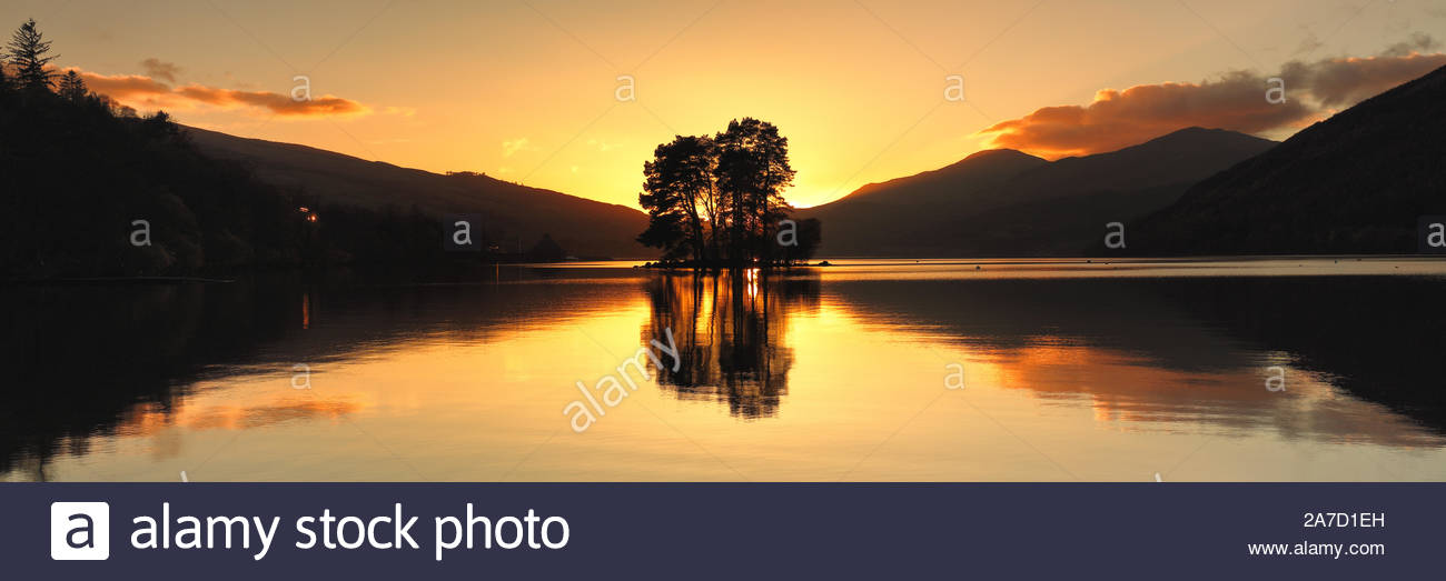 Il sole che tramonta dietro un'isola di alberi da Loch Tay da Perth and Kinross, Scozia. Foto Stock