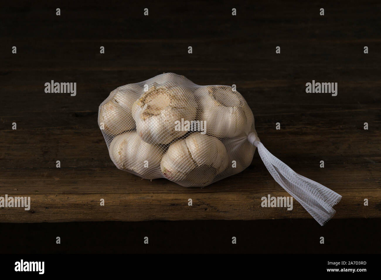 Bulbi di aglio in un bianco sacchetto di nylon su un marrone la superficie in legno Foto Stock
