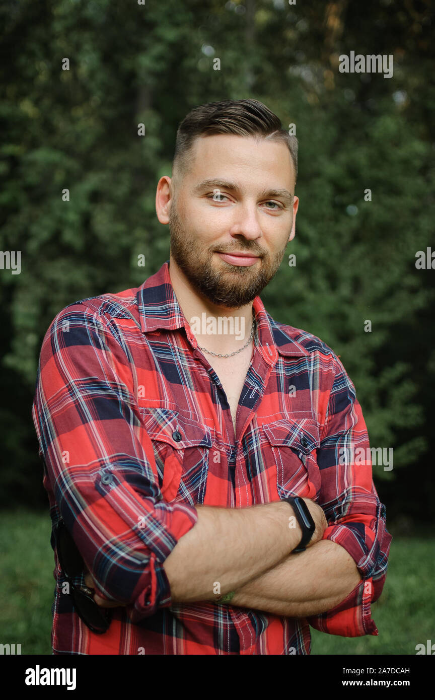 Ritratto all'aperto di rilassata bel giovane uomo con la barba nel parco su alberi verde dello sfondo. Tanga concetto di stile. Foto Stock