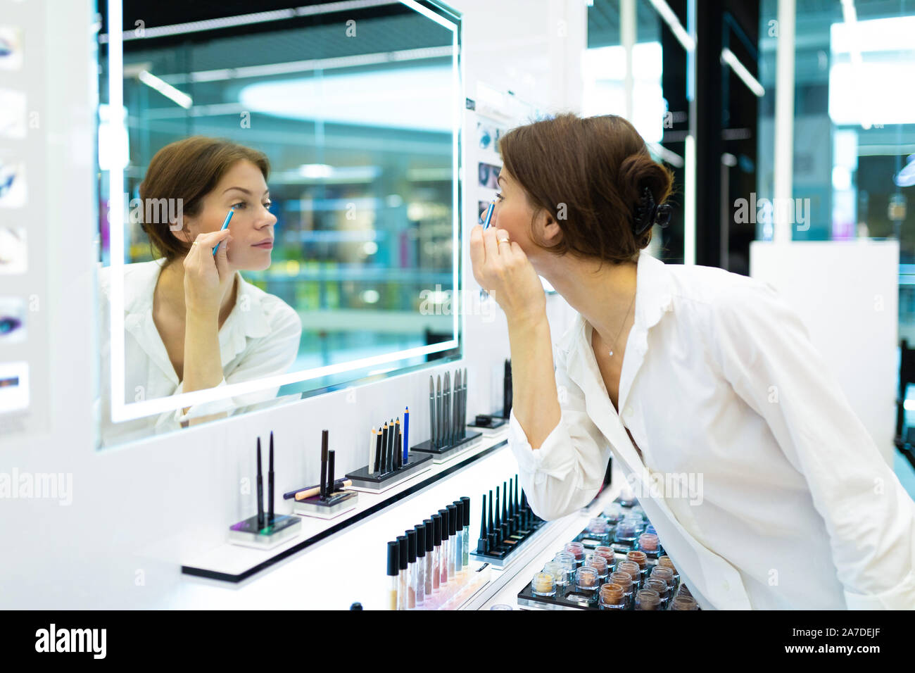 Giovane donna in un negozio di cosmetici è messa sul make-up con blue eye-matita nella parte anteriore dello specchio Foto Stock