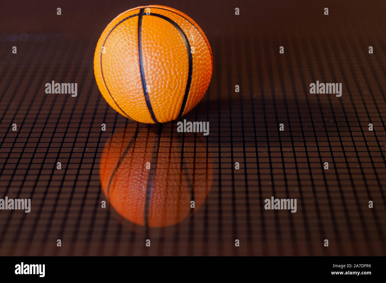Arancione il basket e la sua immagine riflessa al buio su un fondo a scacchi Foto Stock