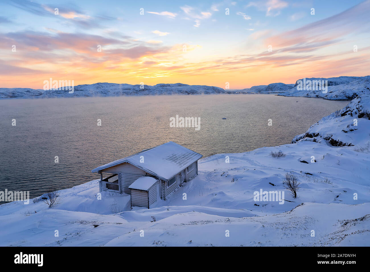 Una casa in legno, il mare di Barents all'alba in Teriberka, Regione di Murmansk, la penisola di Kola. La Russia. Forte nebbia o fumo di mare. Foto Stock