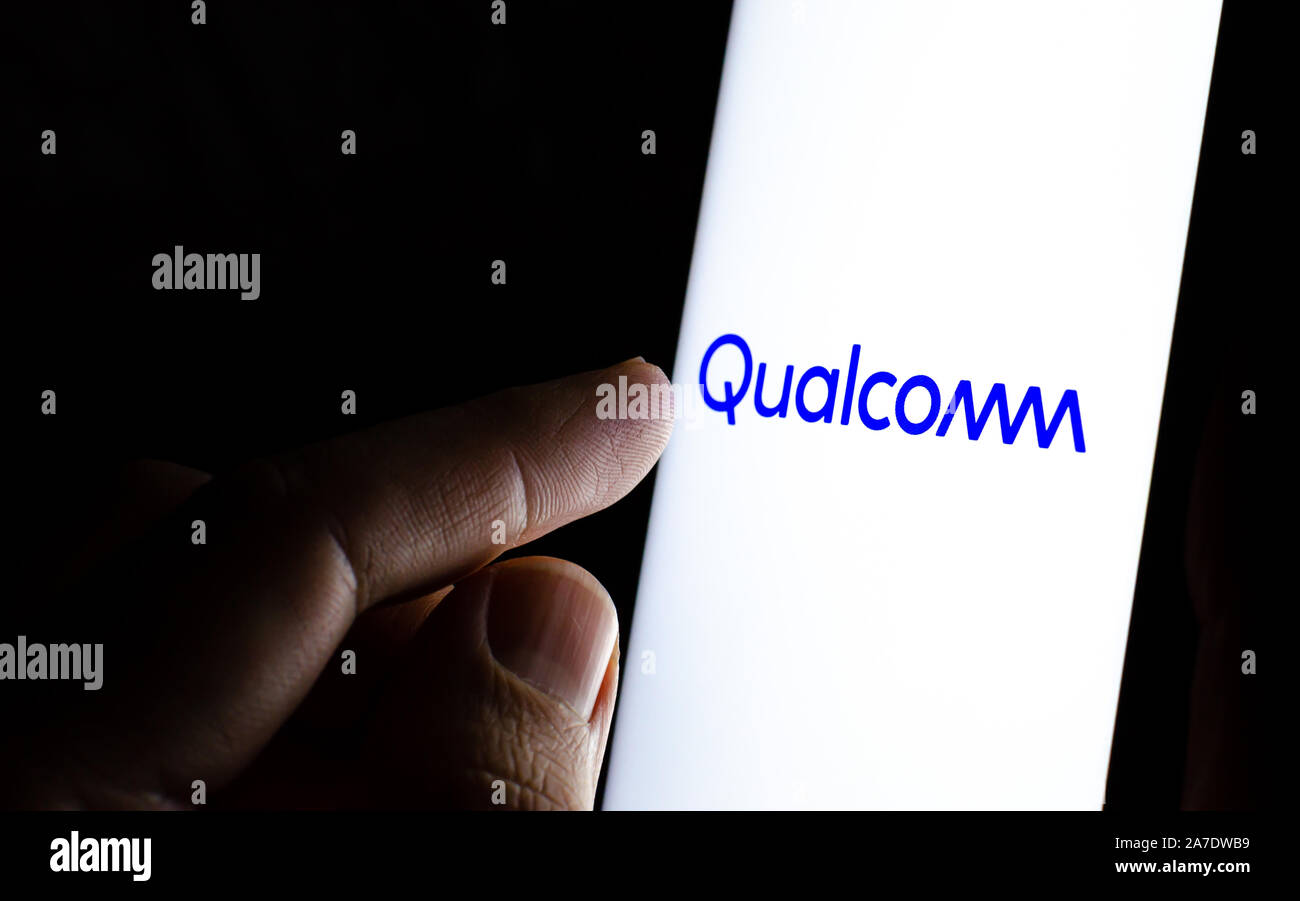 Qualcomm logo su una schermata dello smartphone in una stanza buia e un dito di toccarlo. Foto Stock