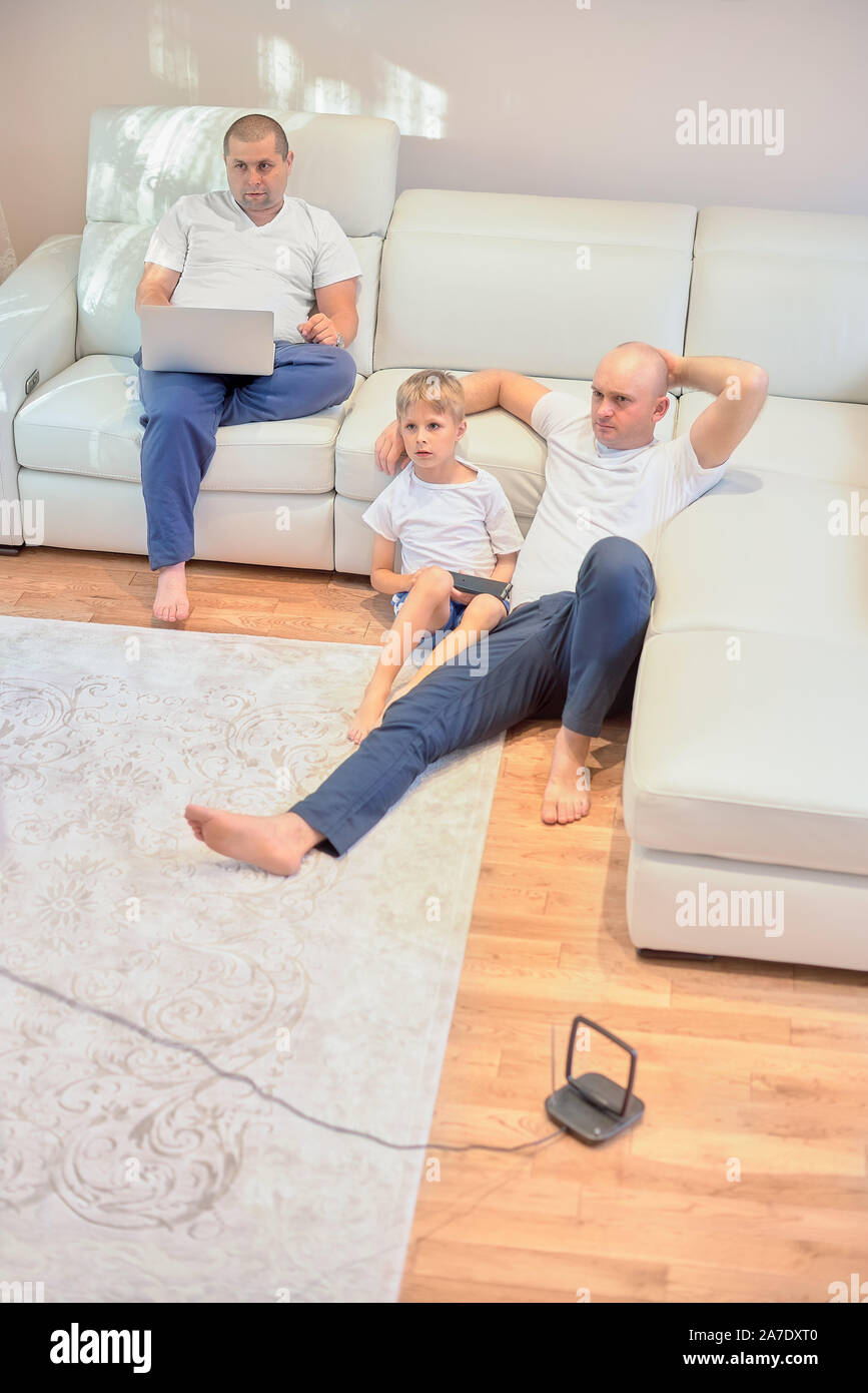 Famiglia giovane guardando la televisione, due ragazzi e un bambino seduto sul divano e pavimento nel salotto di casa. Foto Stock