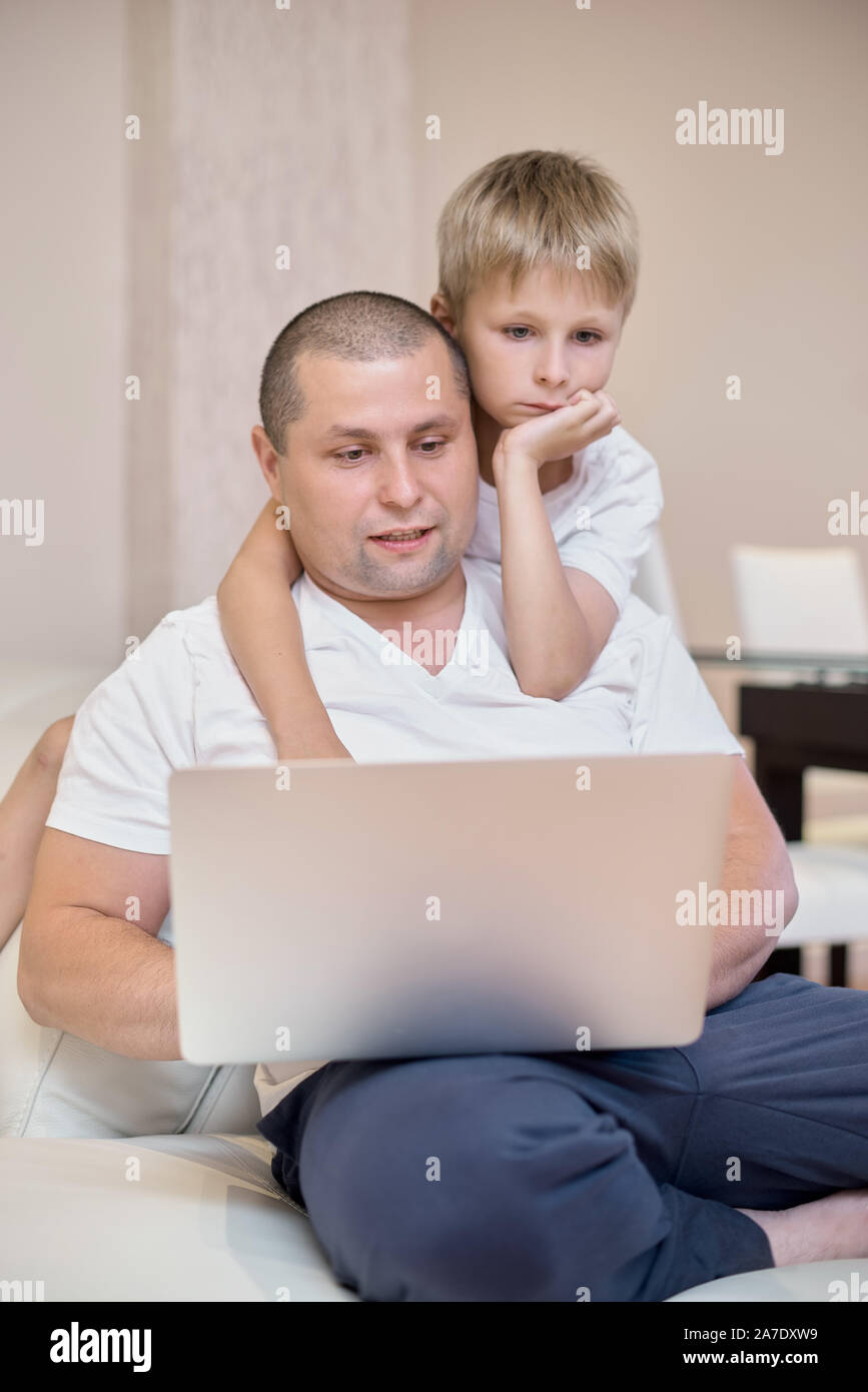 Il figlio e il padre sono seduti sul divano che guardano un notebook, una famiglia felice. Foto Stock