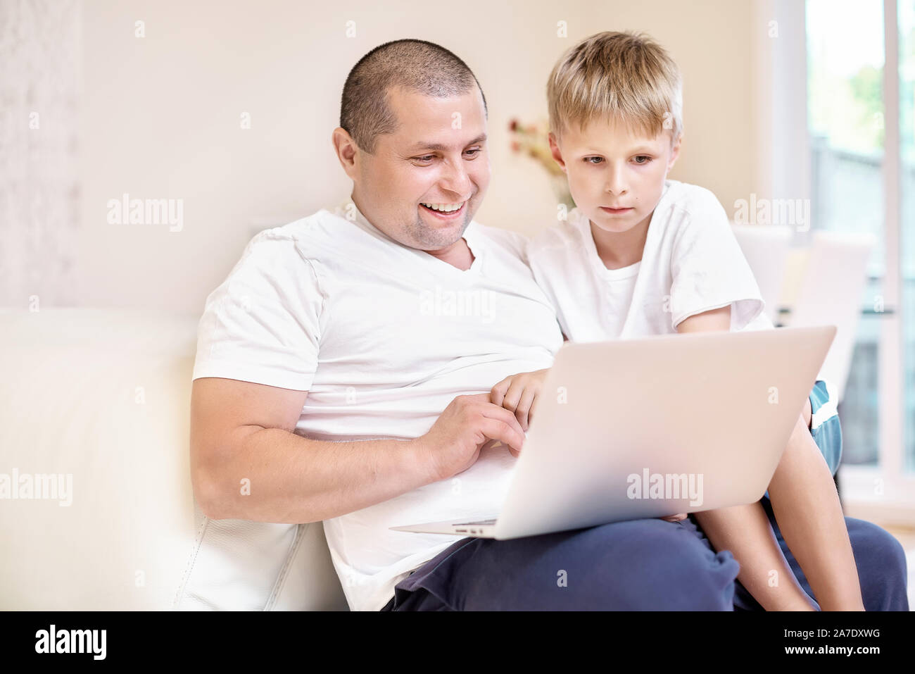 Il figlio e il padre sono seduti sul divano che guardano un notebook, felice emozioni da quello che vide una famiglia felice. Foto Stock
