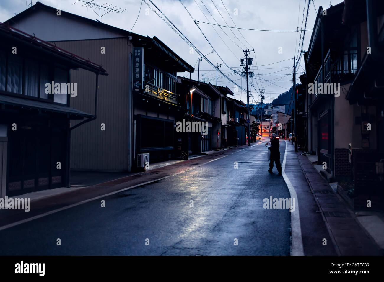 Takayama, Giappone - Aprile 8, 2019: Città nella Prefettura di Gifu nel tradizionale villaggio di notte con la lanterna accesa lampade e donna attraversamento strada Foto Stock