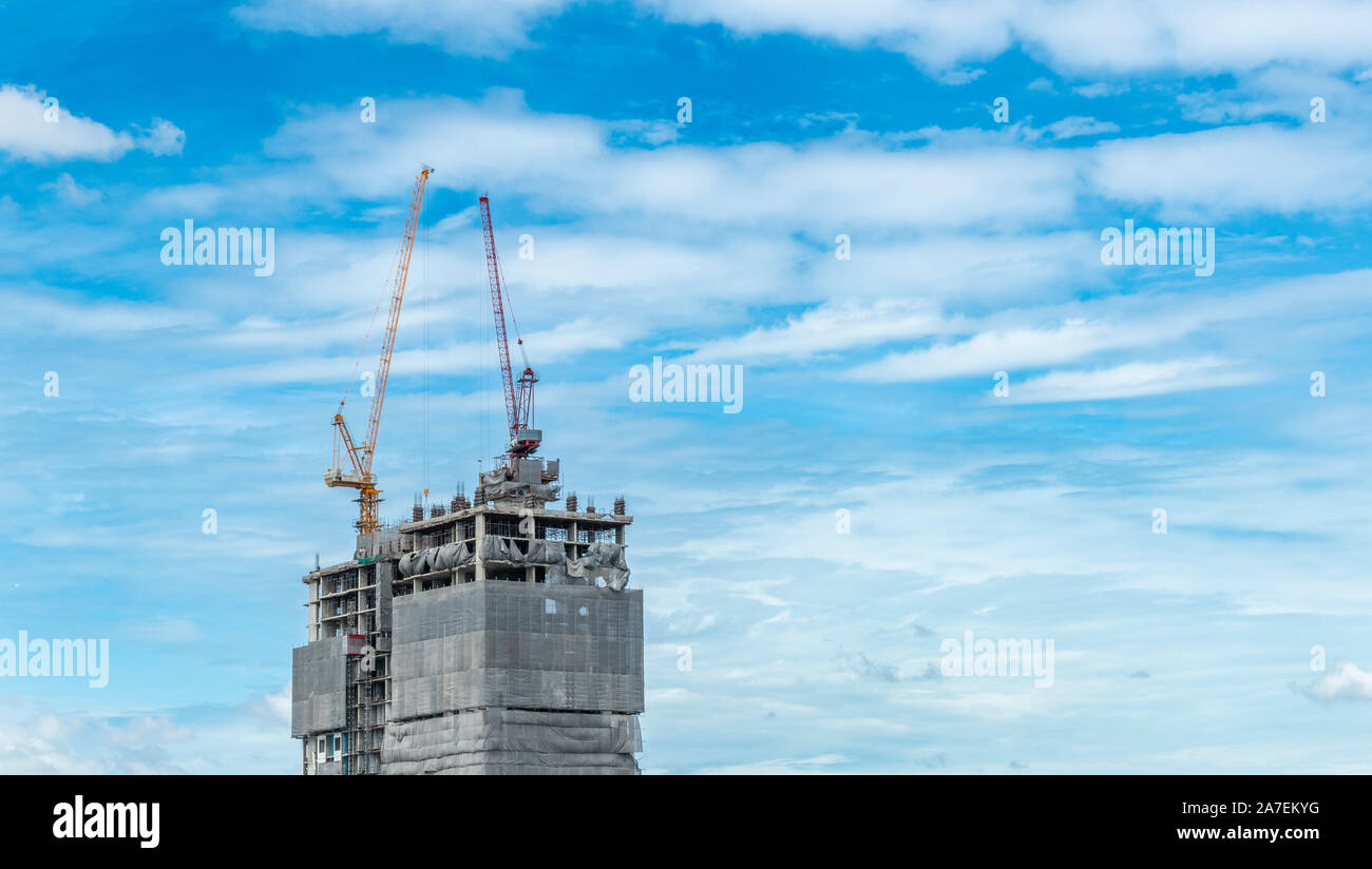Gru a lavorare sulla parte superiore dell edificio, stand alone edificio, cielo blu e nuvole sullo sfondo Foto Stock