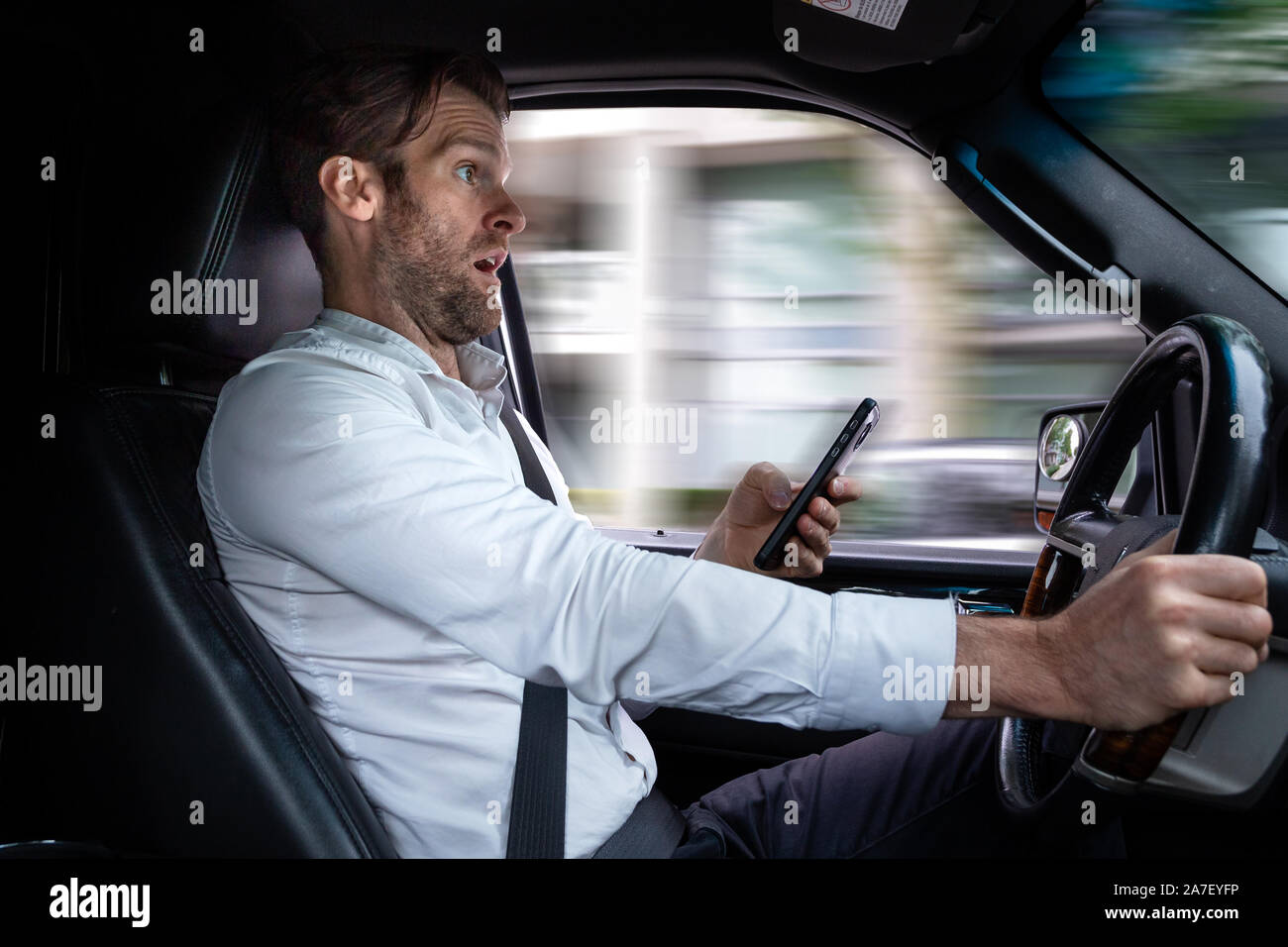 Un uomo caucasico di mezza età distratto durante la guida utilizzando un dispositivo mobile arresta improvvisamente il suo veicolo per evitare un incidente. Foto Stock