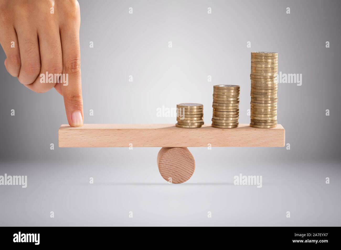Close-up di una persona del dito impilati di bilanciamento di monete d'oro su altalena in legno Foto Stock