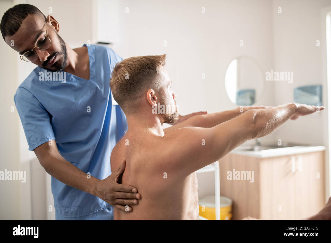 Giovani mixed-gara medico specialista in uniforme il massaggio schiena del paziente Foto Stock