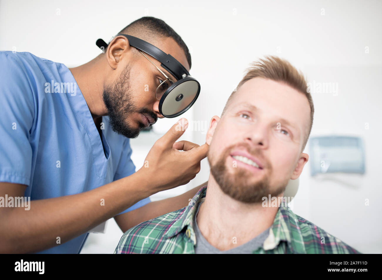 Giovane medico con equipaggiamento speciale sulla testa di esaminare il paziente in ospedale Foto Stock