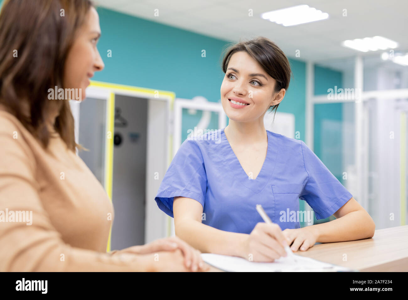 Dottore in uniforme sorridente al paziente durante la consultazione giovane donna nelle cliniche Foto Stock