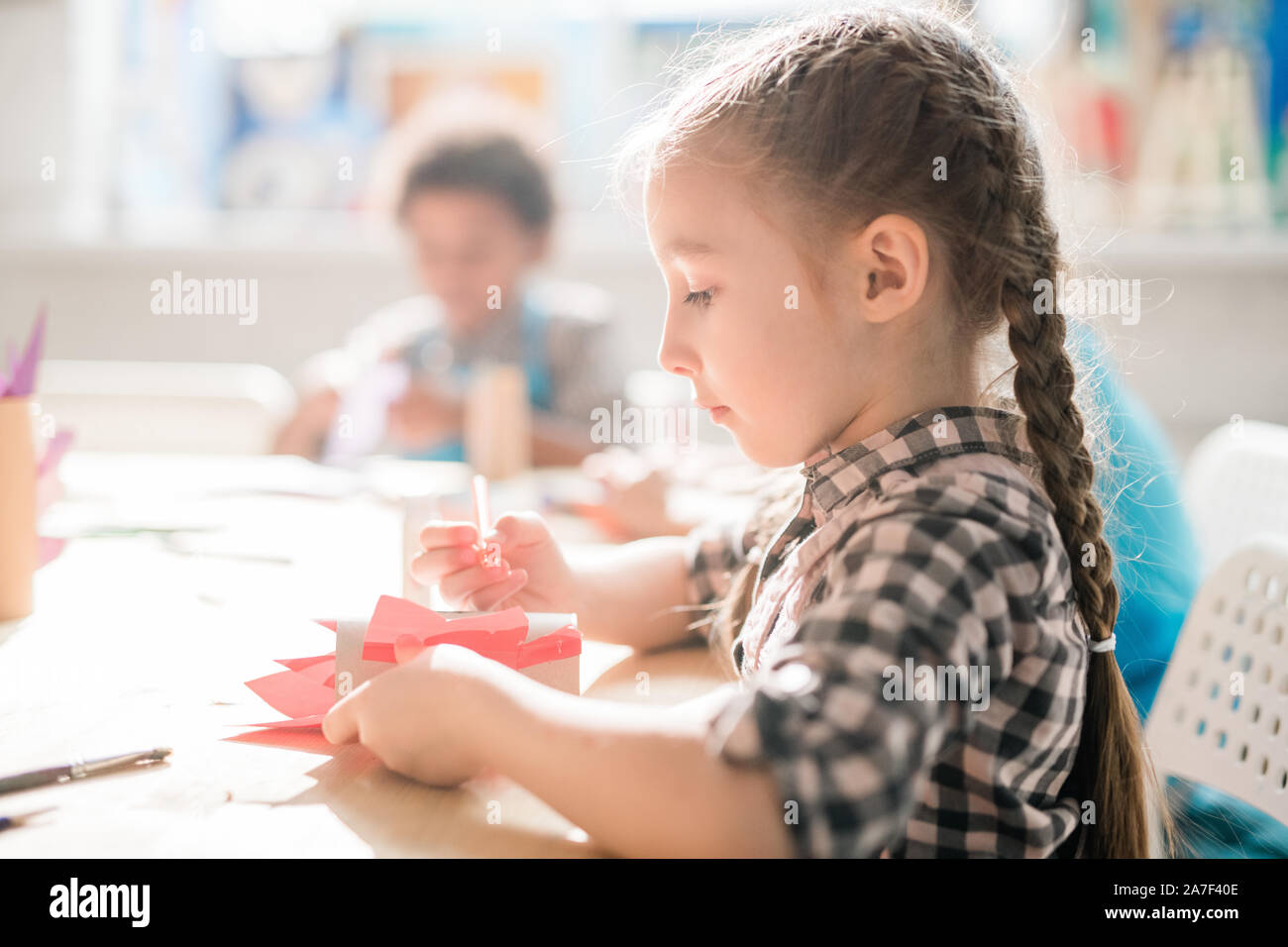 Creative schoolgirl seduto da scrivania e rendendo decorazione o giocattolo a lezione Foto Stock