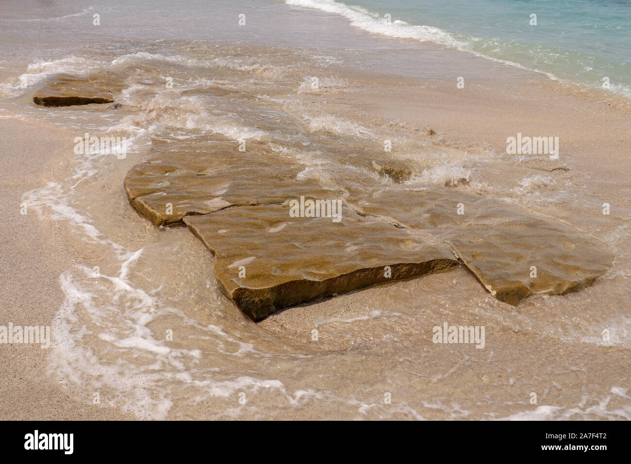 Pietre piatte imitando piastrelle di grandi dimensioni sulla costa dell'Oceano Indiano a vergine spiaggia di Bali. Pezzi di ocra color rocce levigate dal mare surf. Mare schiumoso Foto Stock