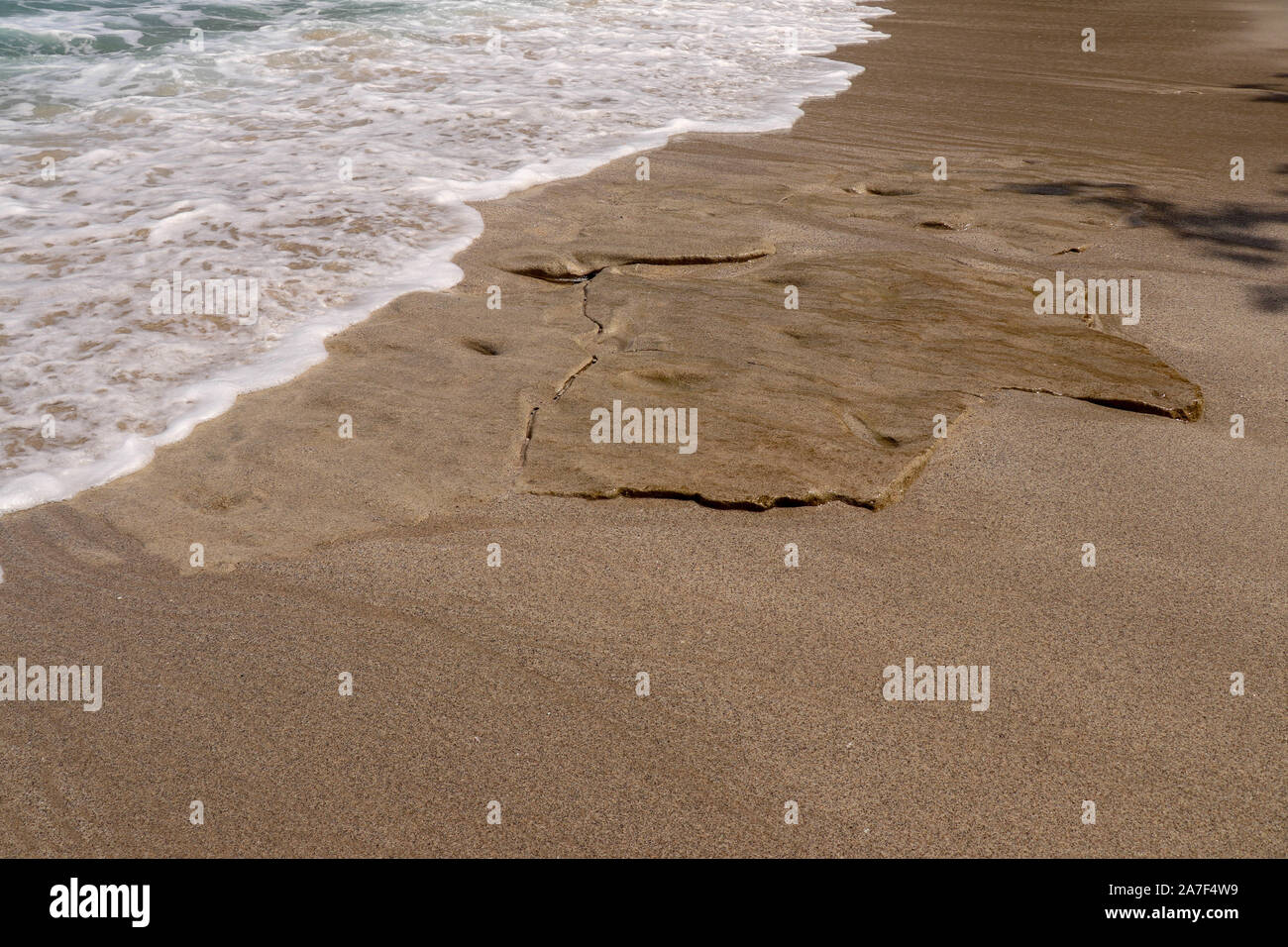 Pietre piatte imitando piastrelle di grandi dimensioni sulla costa dell'Oceano Indiano a vergine spiaggia di Bali. Pezzi di ocra color rocce levigate dal mare surf. Mare schiumoso Foto Stock