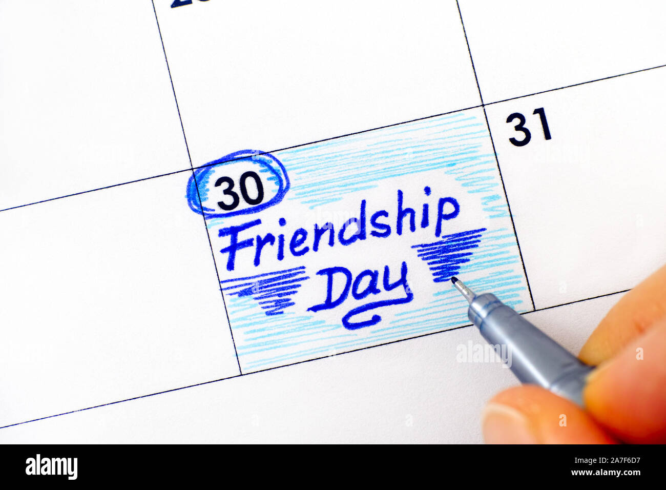 Dita di donna con penna scrittura promemoria amicizia giorno nel calendario. Luglio 30. Foto Stock