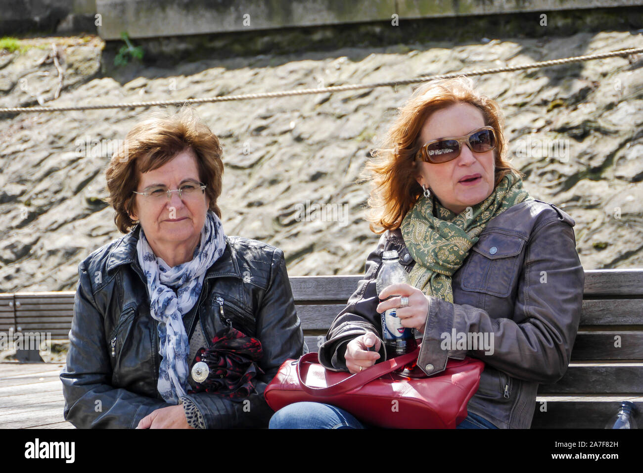 Realistico ritratto di due donne di mezza età seduti sulla pubblica banco all'aperto. Medium Shot. Foto Stock