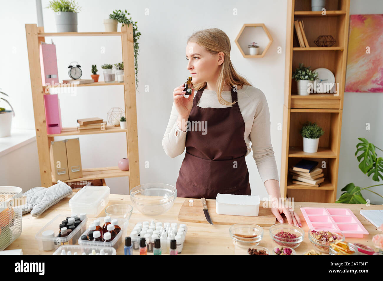 Bionda e giovane femmina nel grembiule marrone odore di essenza aromatica in bottiglia piccola Foto Stock