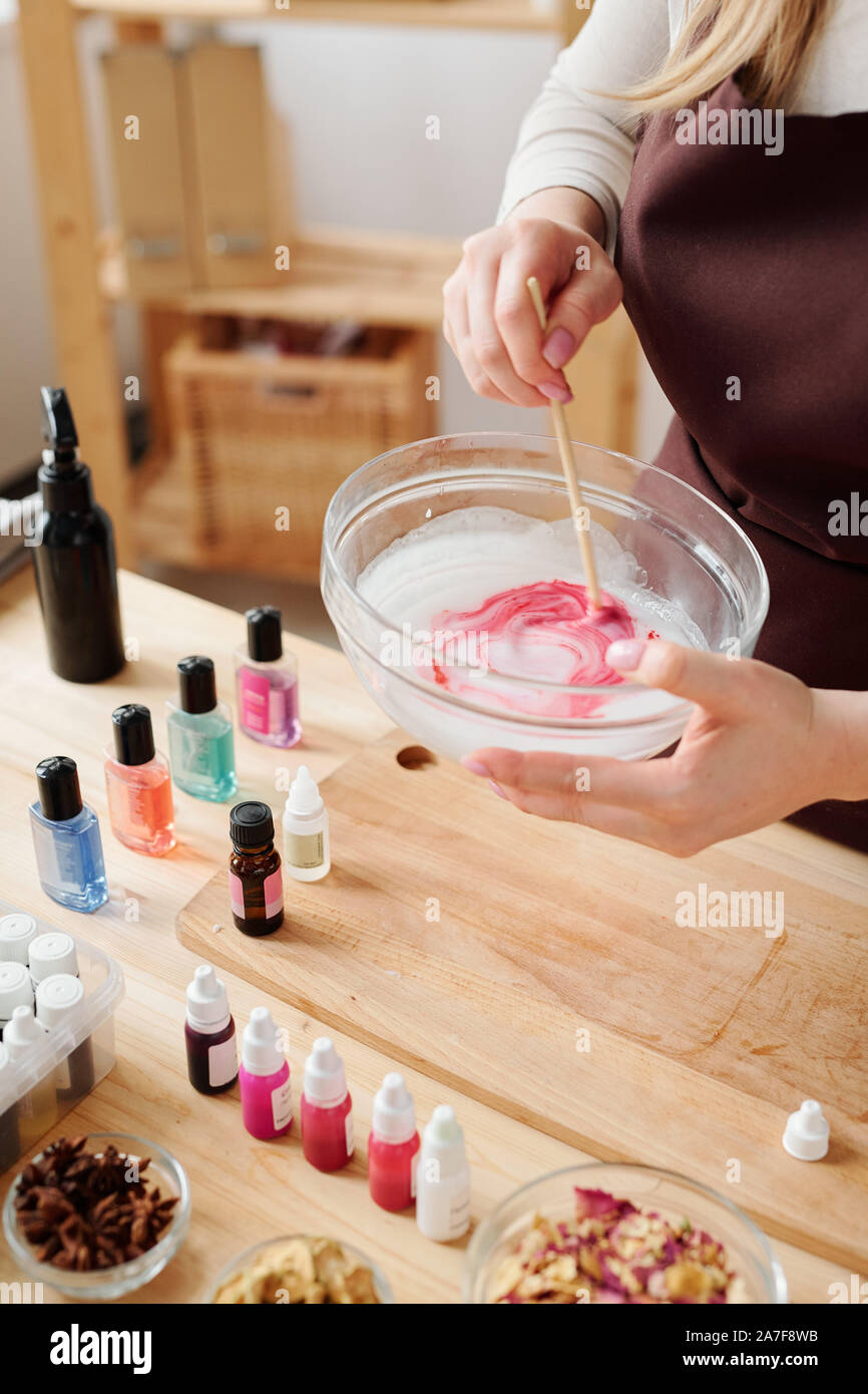 Mani di craftswoman liquido di miscelazione la massa di sapone con colore rosso cremisi in vetreria Foto Stock