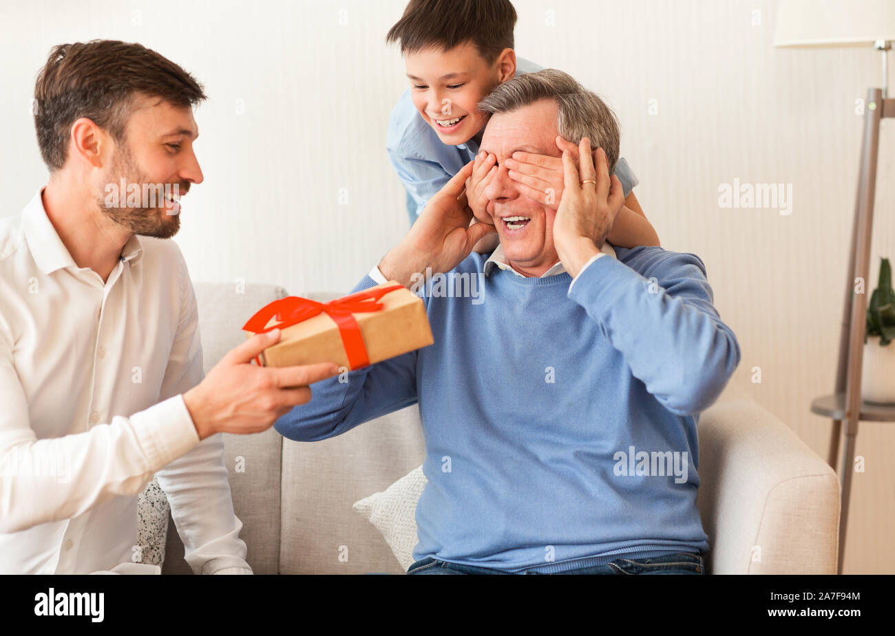 Coppia, figlio e nipote nonno Congratulazioni dando confezione regalo Indoor Foto Stock