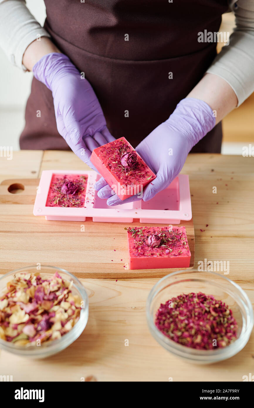 Le mani della giovane donna in lilla guanti barra di contenimento di prodotti freschi fatti a mano sapone floreale Foto Stock