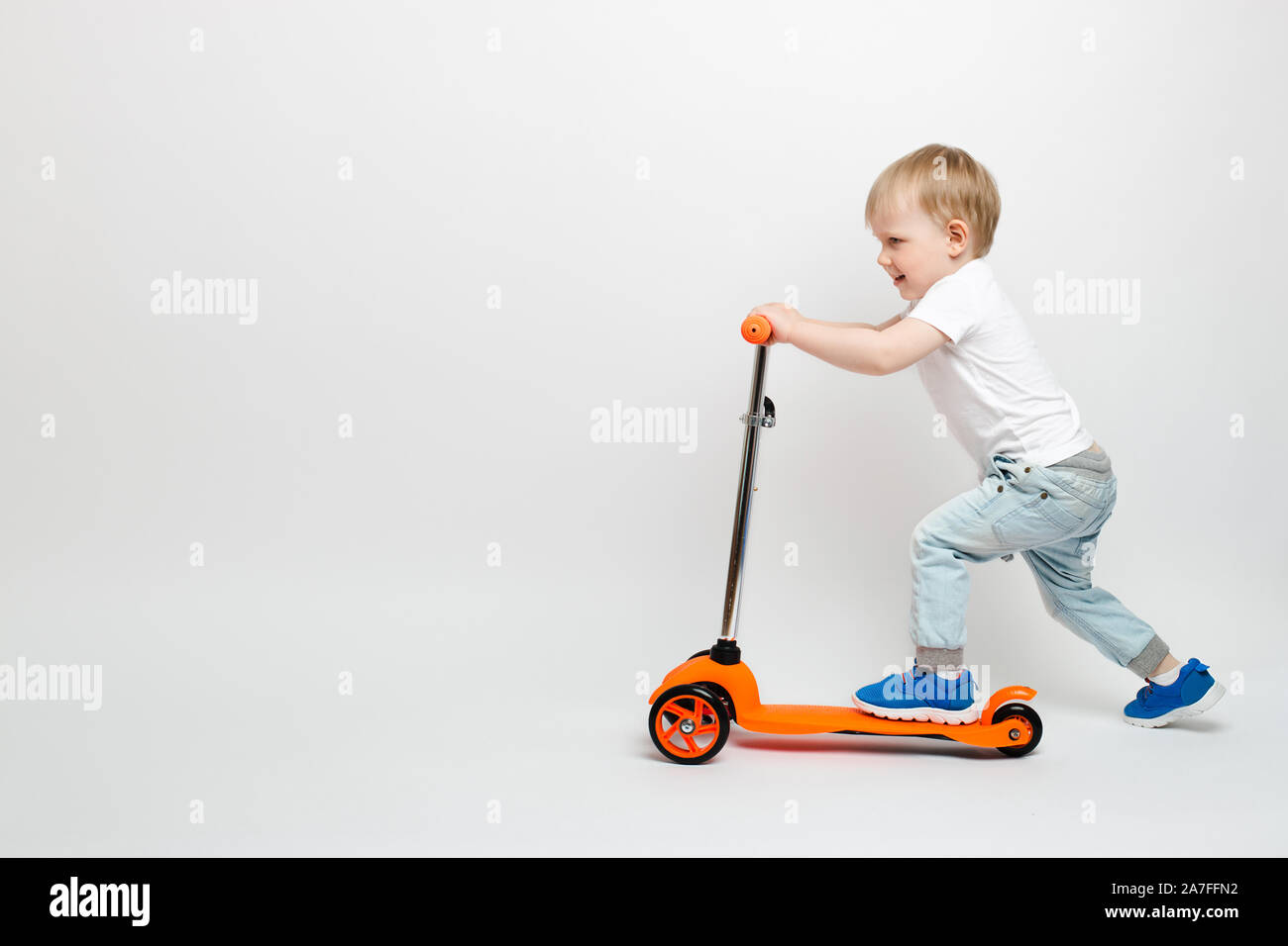 Bimbi felici bambino in jeans cavalca un scooter arancione su sfondo bianco  in studio. Concetto per la pubblicità di giocattoli per bambini con spazio  per il testo Foto stock - Alamy