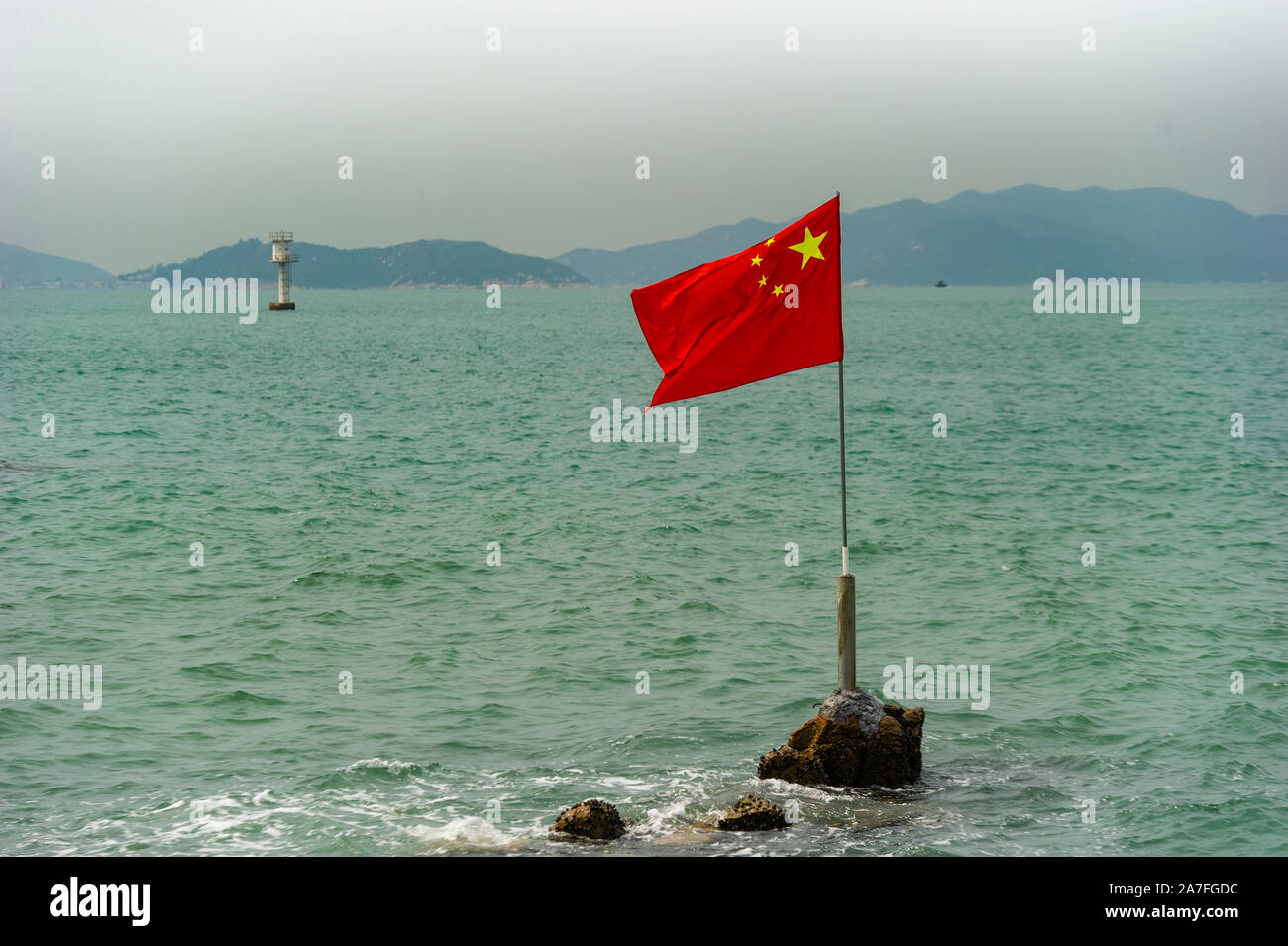 La bandiera cinese vola da una roccia in mare dal consorzio Lamma Island, Hong Kong, rafforzare il messaggio che Hong Kong è territorio cinese Foto Stock