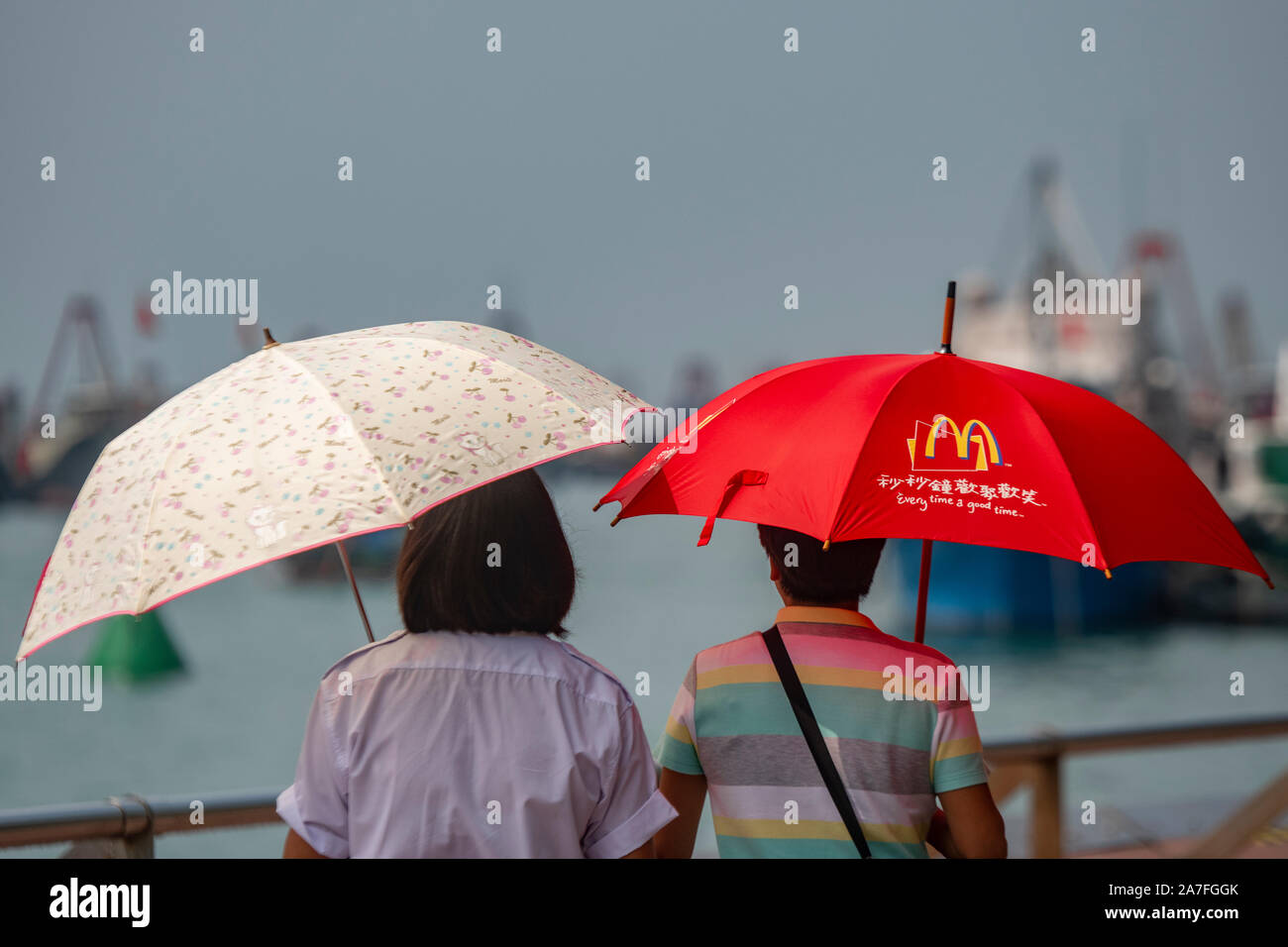 Una donna cinese porta un McDonalds ombrello con scrittura cinese di Hong Kong Foto Stock