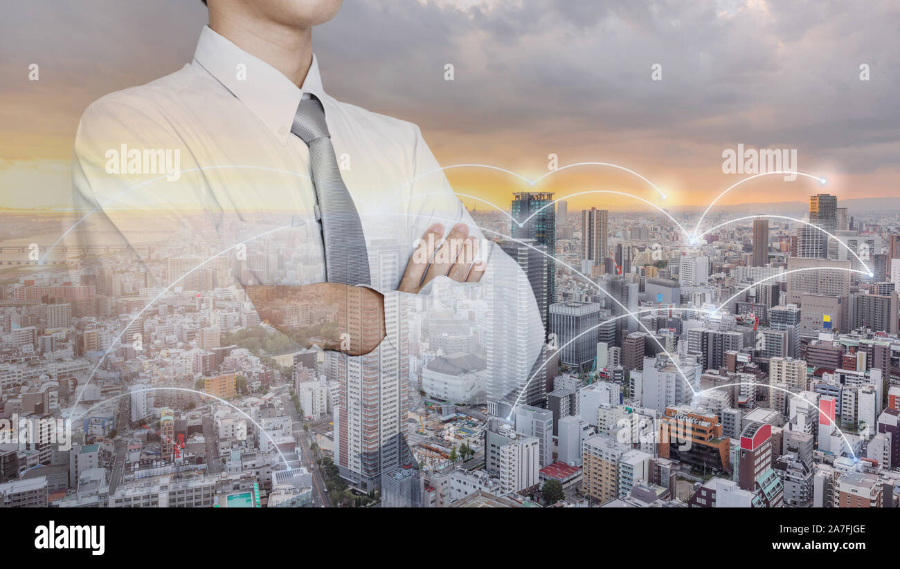 Imprenditore in camicia bianca con braccio incrociati, con la città moderna e connessione di rete Foto Stock