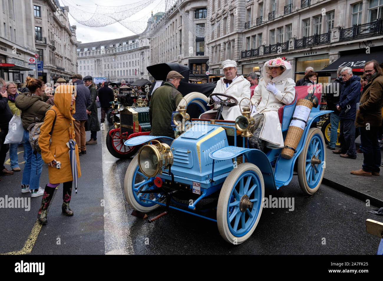 Westminster, Inghilterra, Regno Unito. 2 Novembre 2019.Il Regent Street Motor Show, un evento per la presentazione di 125 anni di veicolo motoristico tenutosi oggi su nuvoloso giorno. L'evento includono molti dei veicoli e il partecipante dalla Bonham auto run che si terrà domani a Londra. Vista globale del giovane in abbigliamento vintage a cavallo di un blu vintage 1902c Peugeot con i visitatori che desiderano. Foto Stock