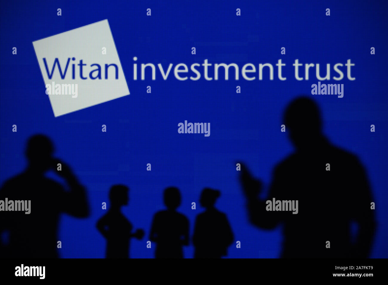 Il Witan Investment Trust logo è visibile su uno schermo a LED in background mentre si profila una persona utilizza uno smartphone (solo uso editoriale) Foto Stock