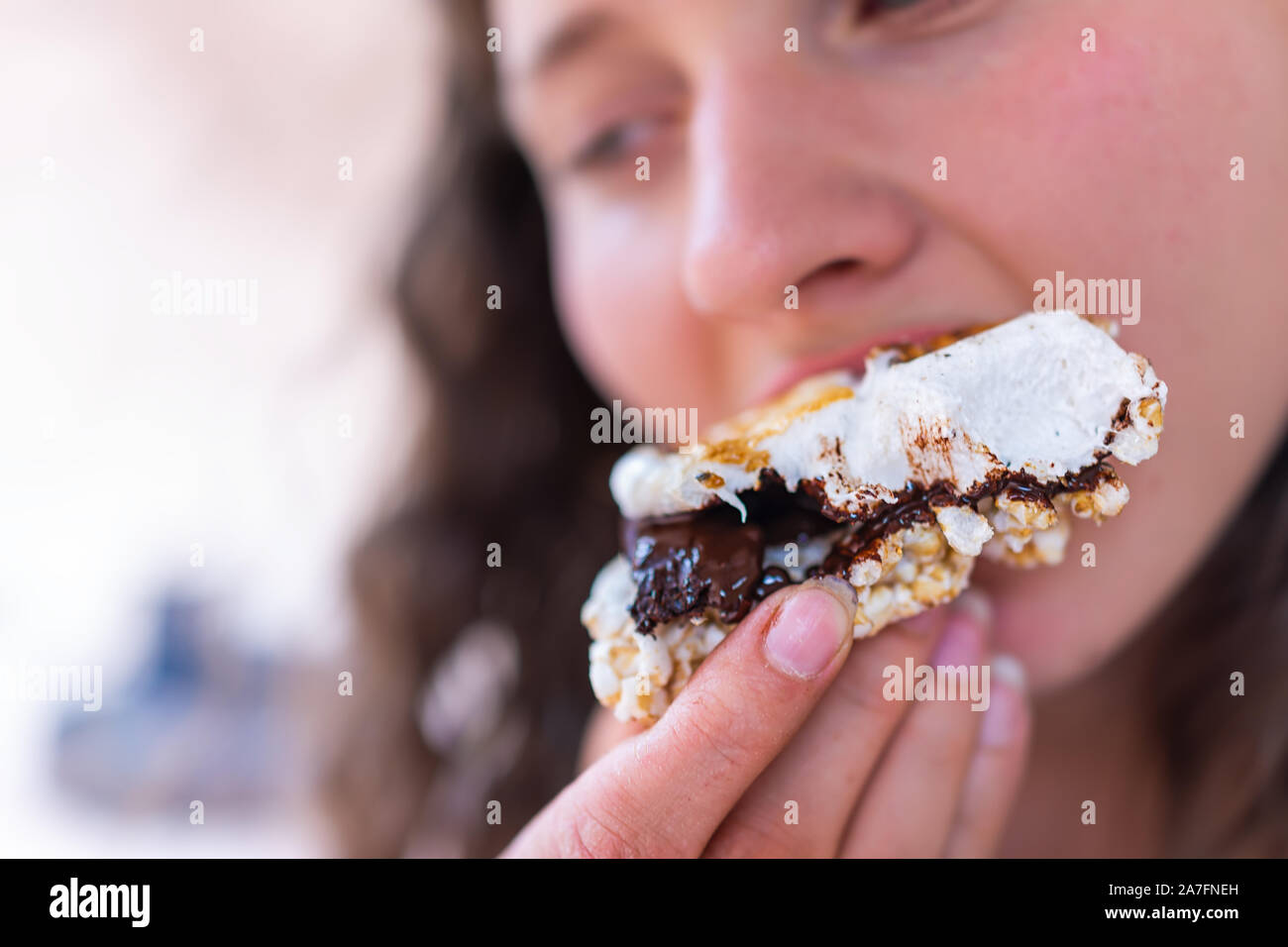 Macro Closeup della ragazza giovane mangiare gooey arrosto di marshmallows smores con cioccolato e torta di riso cracker dal fuoco in campeggio campfire grill Foto Stock