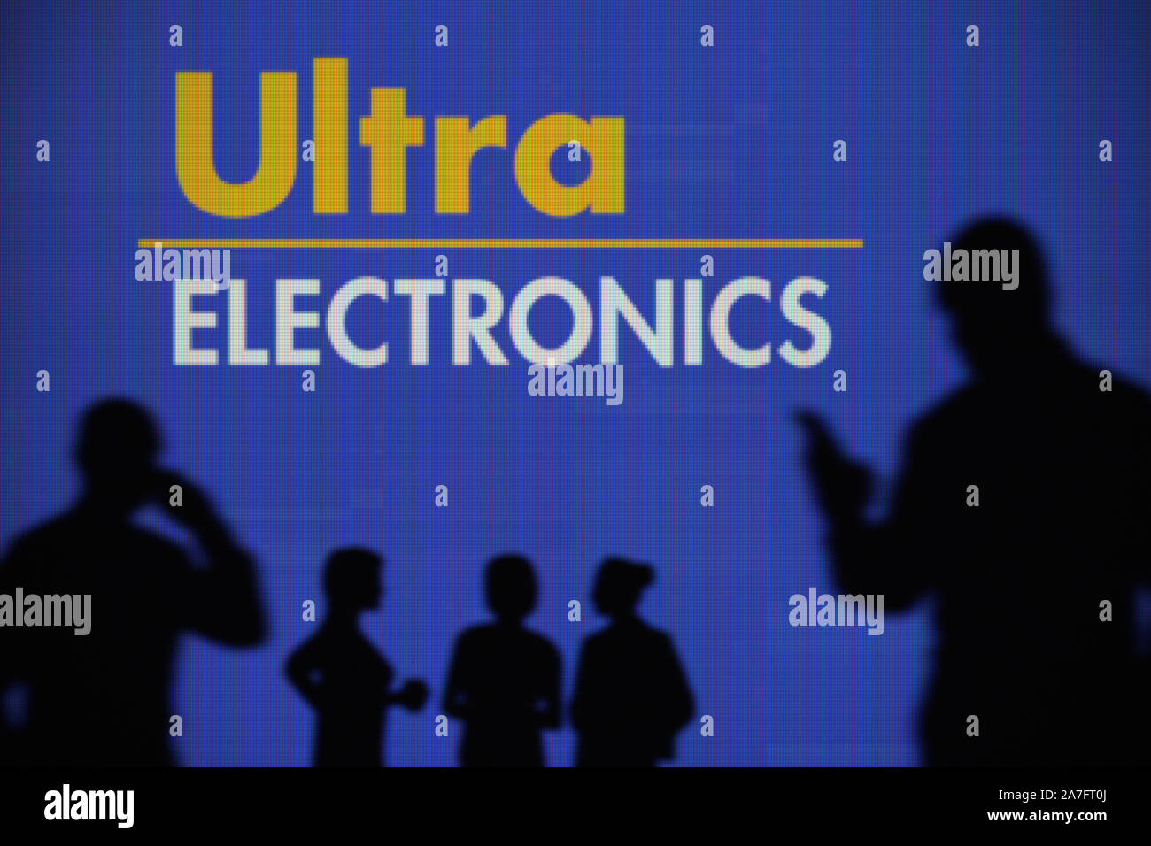 L'Ultra Electronics logo è visibile su uno schermo a LED in background mentre si profila una persona utilizza uno smartphone (solo uso editoriale) Foto Stock