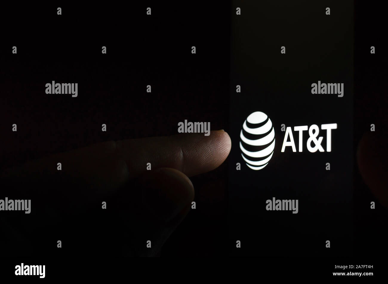 AT&T logo su una schermata dello smartphone in una stanza buia e un dito di toccarlo. Foto Stock