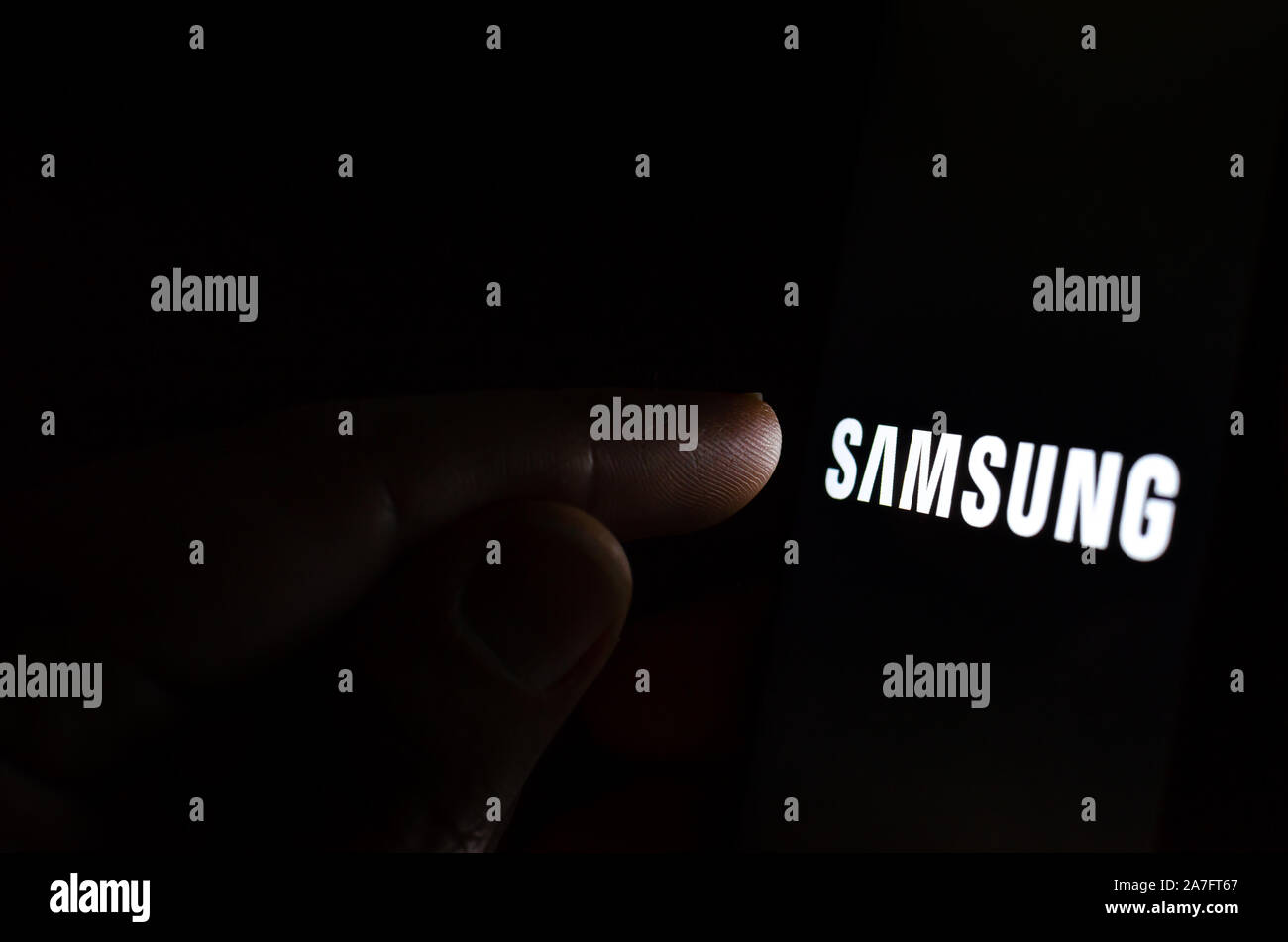 Logo Samsung su una schermata dello smartphone in una stanza buia e un dito di toccarlo. Foto Stock