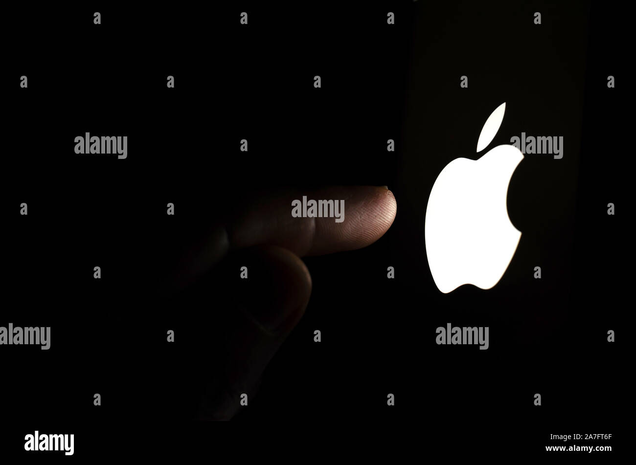 Il logo Apple su una schermata dello smartphone in una stanza buia e un dito di toccarlo. Foto Stock