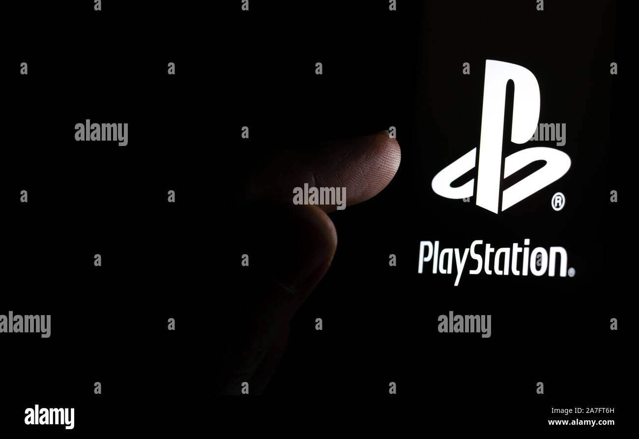 Il logo PlayStation su una schermata dello smartphone in una stanza buia e un dito di toccarlo. Foto Stock
