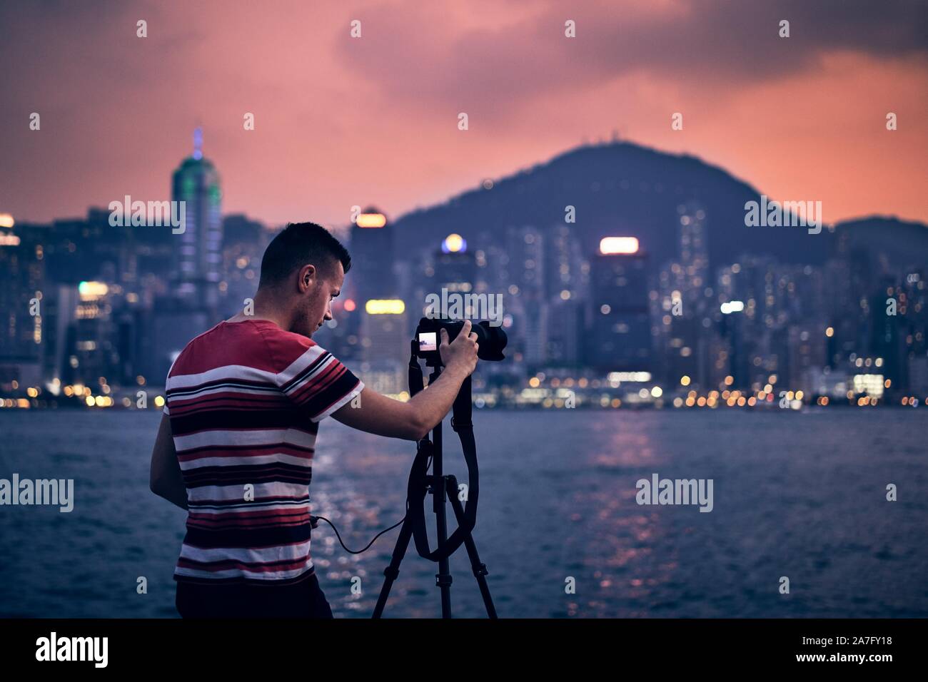 Giovane fotografo (traveler) con treppiede fotografare urban skyline al tramonto, Hong Kong. Foto Stock