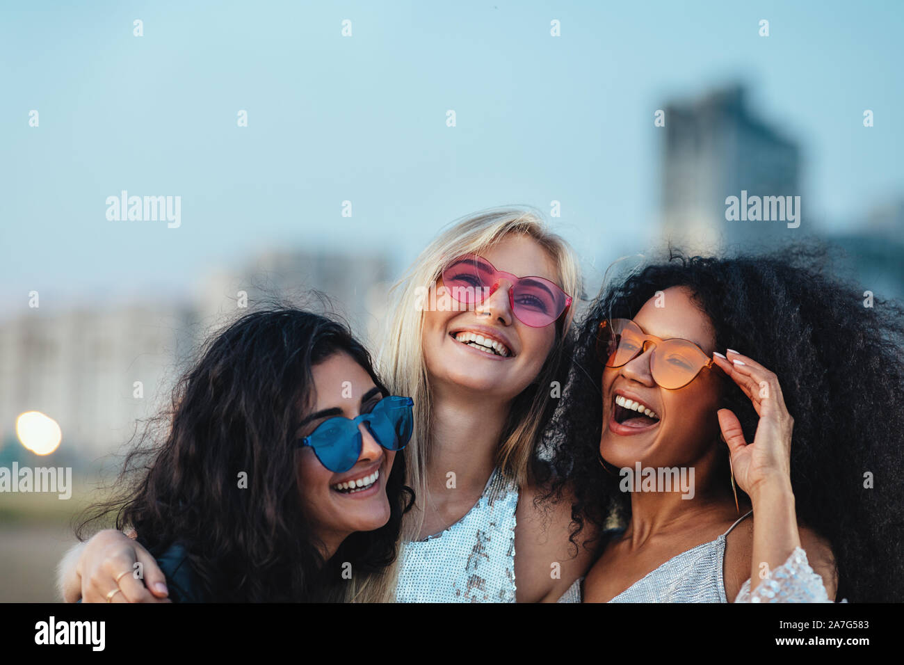 Tre belle donne con occhiali da sole colorati in piedi alla serata all'aperto Foto Stock