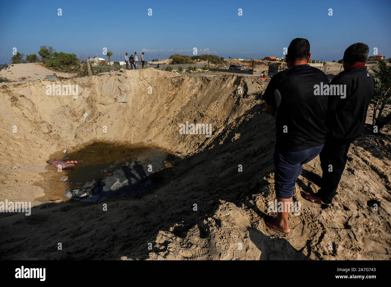 Gli uomini palestinesi guardare un grande cratere dopo un attacco aereo israeliano ha lanciato in risposta al lancio di missili nel sud della striscia di Gaza. Foto Stock