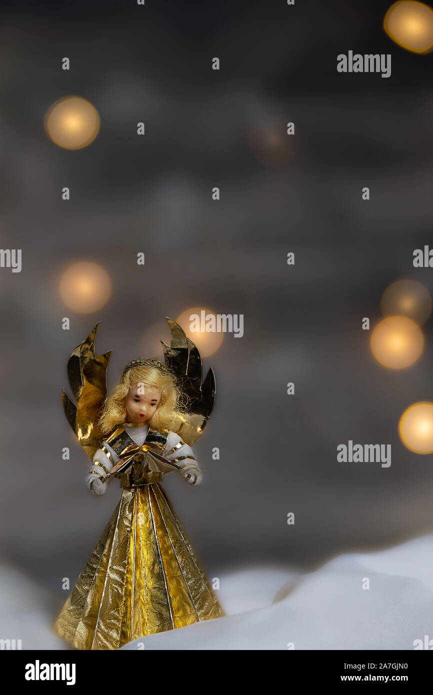 Similrame artigianali di angelo con un libro in mano a pregare e cantare i canti natalizi macchie di luce sul retro Foto Stock