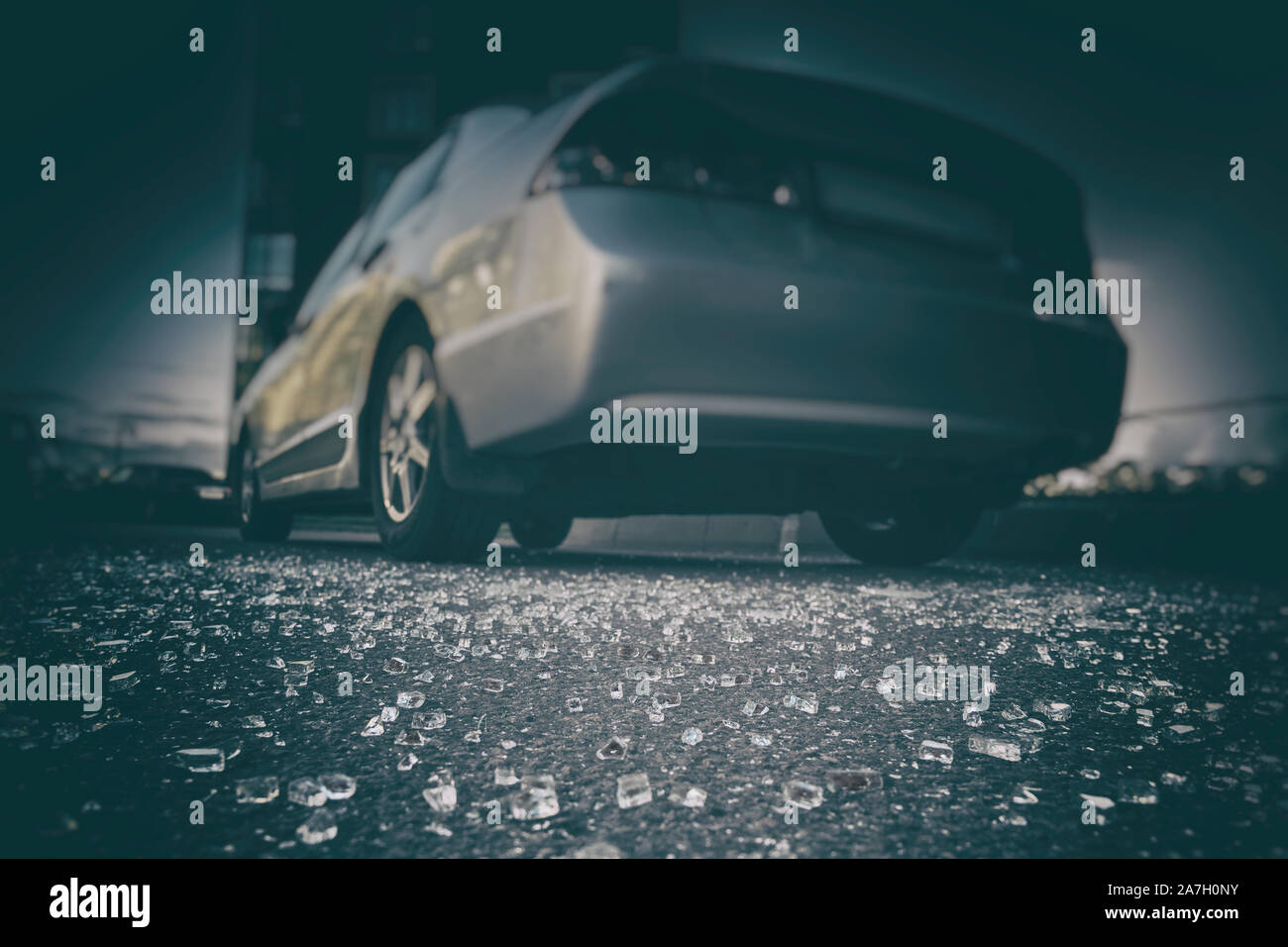 I frammenti di vetro sparsi su asfalto da rottura vetro per auto, concetto di atti di vandalismo Foto Stock