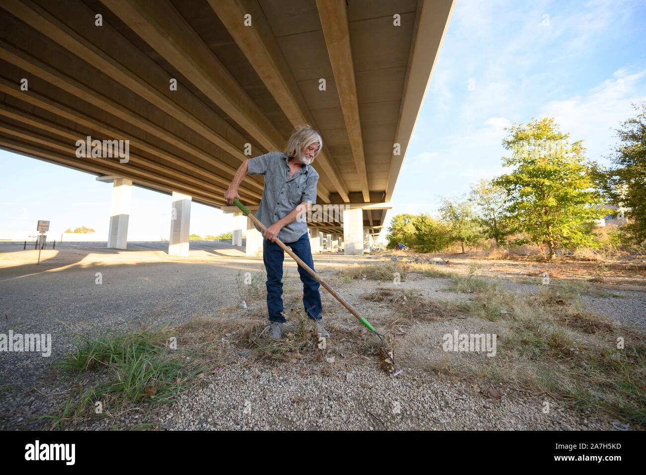 Dopo Texas Gov. Greg Abbott ha annunciato un giro di vite sulla accampamenti in spazi pubblici, un uomo pulisce l'area sotto una Austin, Texas, autostrada sopraelevata dove lui e altri hanno impostato un accampamento provvisorio per i senzatetto. Foto Stock